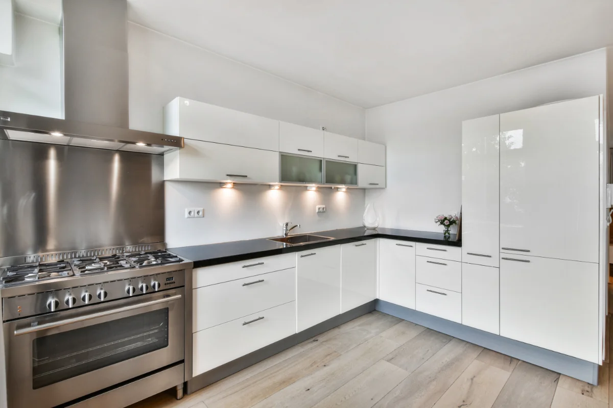 Modern white kitchen with stainless steel stove and hood, black countertop, and tall white cabinets.
