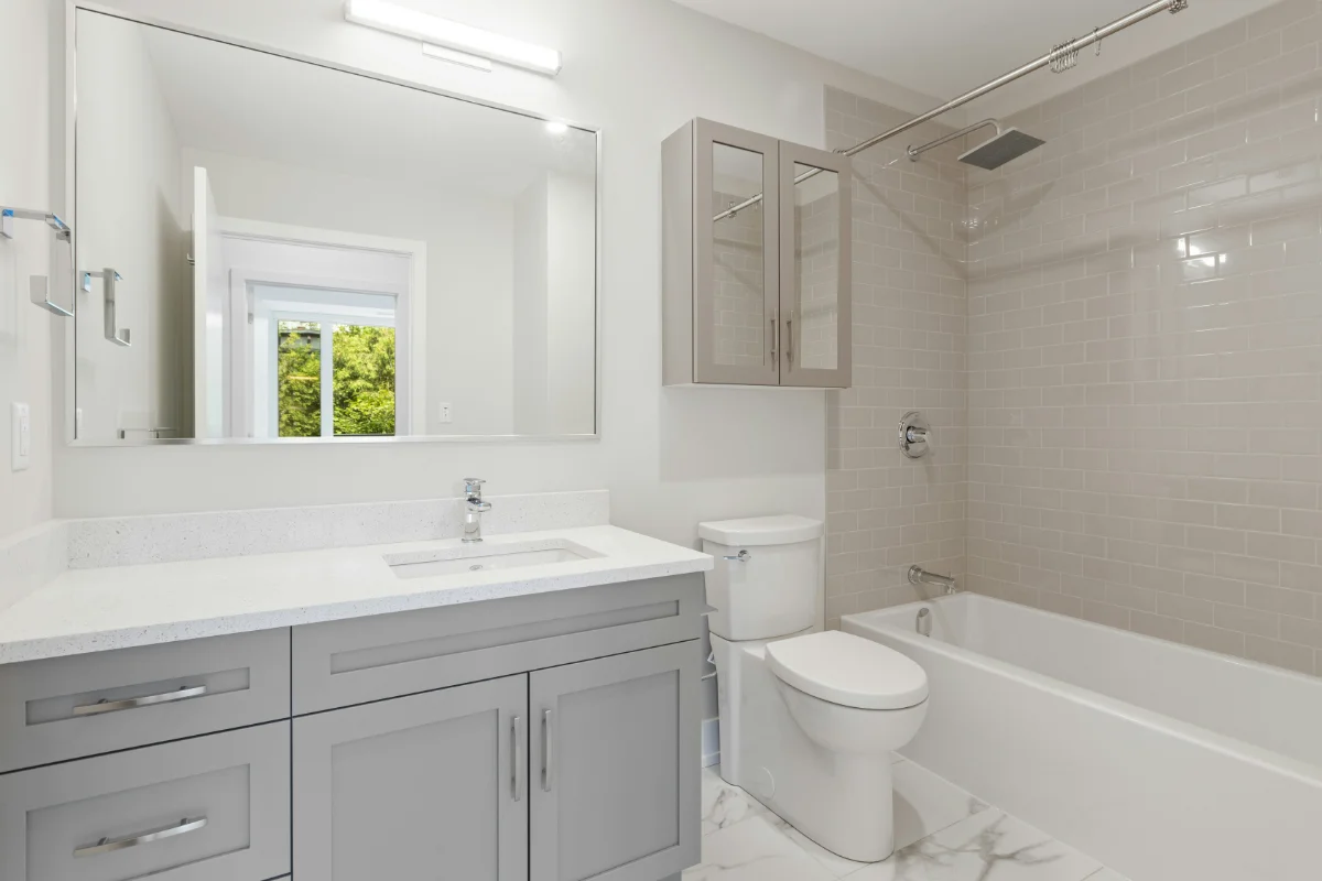 Modern bathroom with gray vanity, white countertop, toilet, and a tiled tub/shower area with chrome fixtures